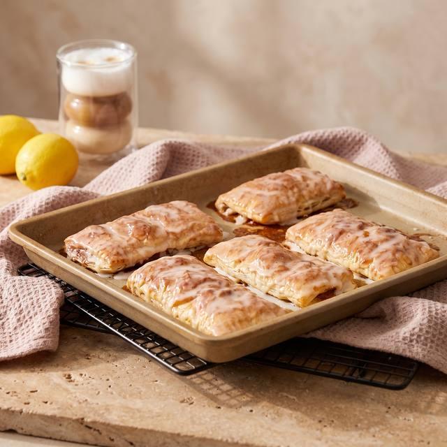 Glasierte Apfeltaschen aus Croissantteig auf dem Pampered Chef® Großen Ofenzauberer Plus, daneben Zimtstangen und Zitronen