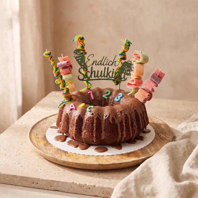 Schoko-Gugelhupf mit glänzender Glasur, bunter Süßigkeiten-Deko und Zucker-Buchstaben zur Einschulung – Pampered Chef® Rezept