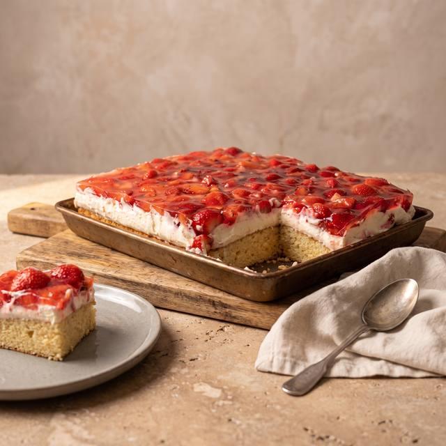 Erdbeerkuchen mit Vanille-Schmand-Creme auf dem Pampered Chef® Großen Ofenzauberer, dahinter ein angeschnittenes Stück auf einem Teller
