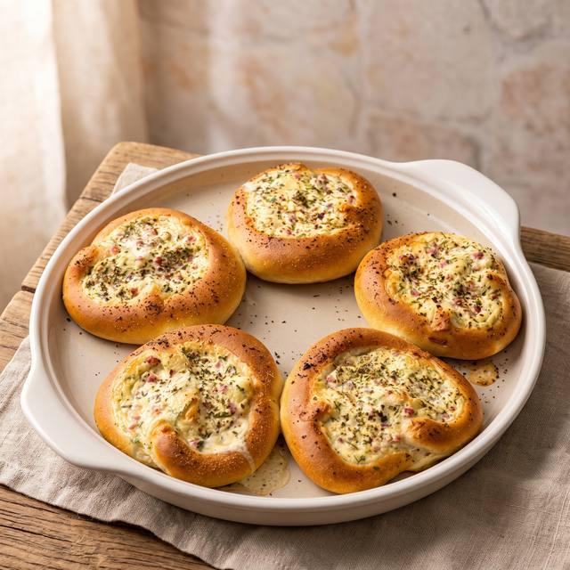 Fünf goldbraun gebackene, gefüllte Laugenbrezeln mit Schmand-Käse-Schinken-Füllung und Schnittlauch auf einem runden Stein – Pampered Chef® Rezept