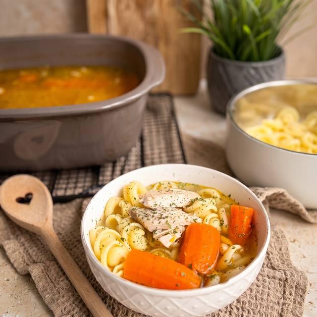 Hühnersuppe mit Hähnchenfleisch, Möhren und Nudeln in einer weißen Schüssel – Pampered Chef® Rezept