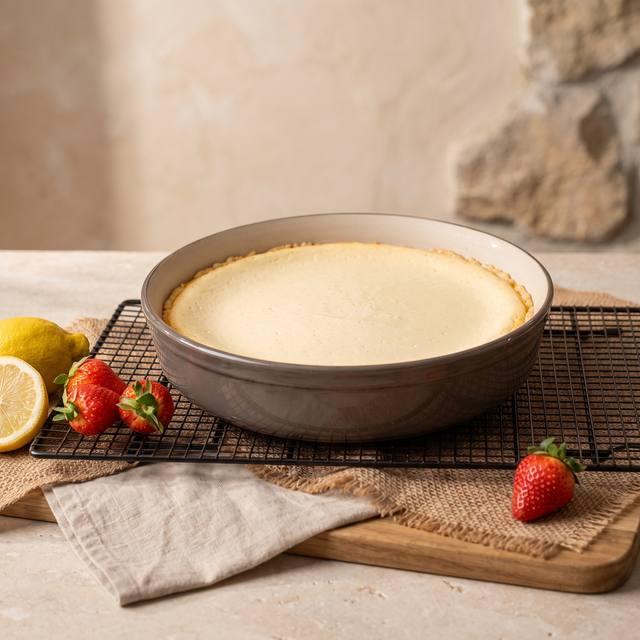 Frisch gebackener Käsekuchen in der Pampered Chef® Runden Ofenhexe, im Hintergrund Zitronen und Erdbeeren