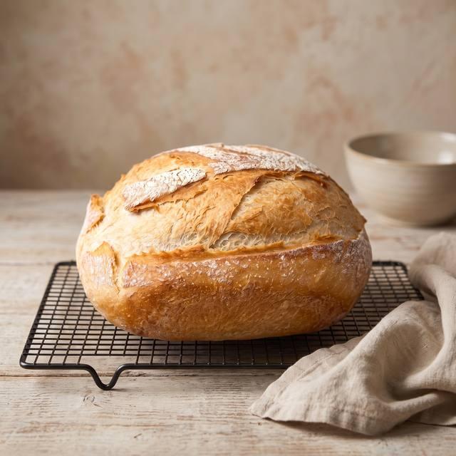 Knuspriges selbstgebackenes Brot mit bemehlter, eingeschnittener Kruste auf einem Kuchengitter – Pampered Chef® Rezept
