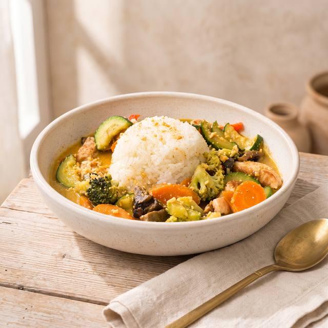 Kokos-Curry mit Hähnchen und Gemüse in einer Schale, mittig Reis und gehackte Erdnüsse darüber gestreut – Pampered Chef® Rezept