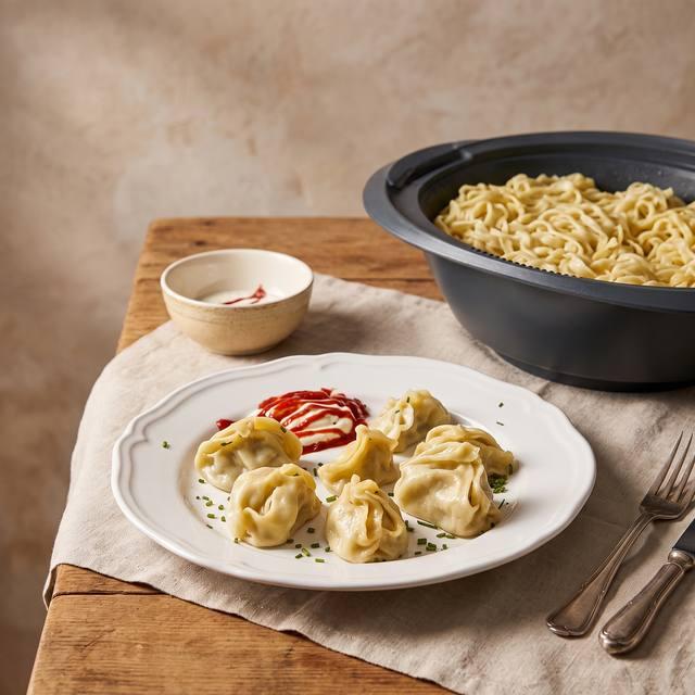 Gedünstete Manti-Teigtaschen mit Hackfleischfüllung auf einem weißen Teller mit Schmand und Ketchup