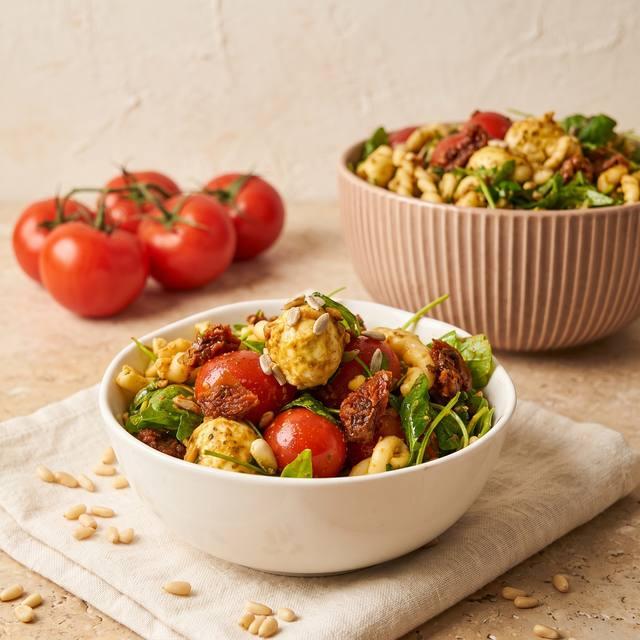 Mediterraner Nudelsalat mit Cherrytomaten, Mozzarellakugeln und Rucola in einer weißen Schüssel