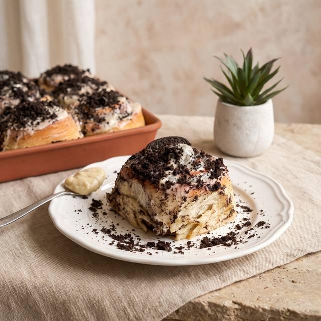 Oreo-Rolls mit cremigem Frischkäse-Frosting und Oreo-Krümeln auf einem Teller, im Hintergrund das Blech mit weiteren Schnecken – Pampered Chef® Rezept