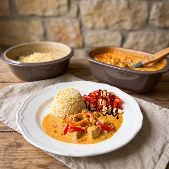Paprika-Sahne-Hähnchen mit Reis auf einem weißen Teller, im Hintergrund zwei Kleine Pampered Chef® Ofenmeister