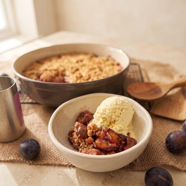 Warmer Pflaumen-Crumble mit Haferflocken-Streuseln, daneben eine Schale mit Vanilleeis – Pampered Chef® Rezept