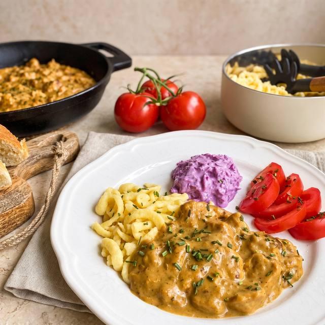 Puten-Geschnetzeltes in cremiger Currysoße mit Spätzle, Rotkohlsalat und Tomaten auf einem Teller – Pampered Chef® Rezept