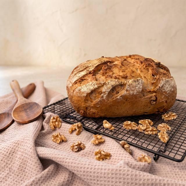 Frisch gebackenes Walnussbrot mit bemehlter, eingeschnittener Kruste auf einem schwarzen Kuchengitter, Walnüsse daneben auf einem Küchentuch – Pampered Chef® Rezept