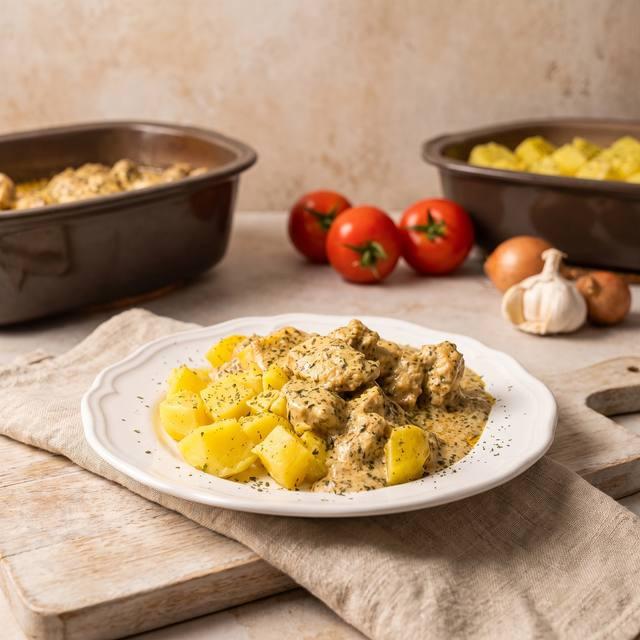 Zwiebel-Sahne-Hähnchen mit Salzkartoffeln auf einem weißen Teller, im Hintergrund zwei Kleine Pampered Chef® Ofenmeister